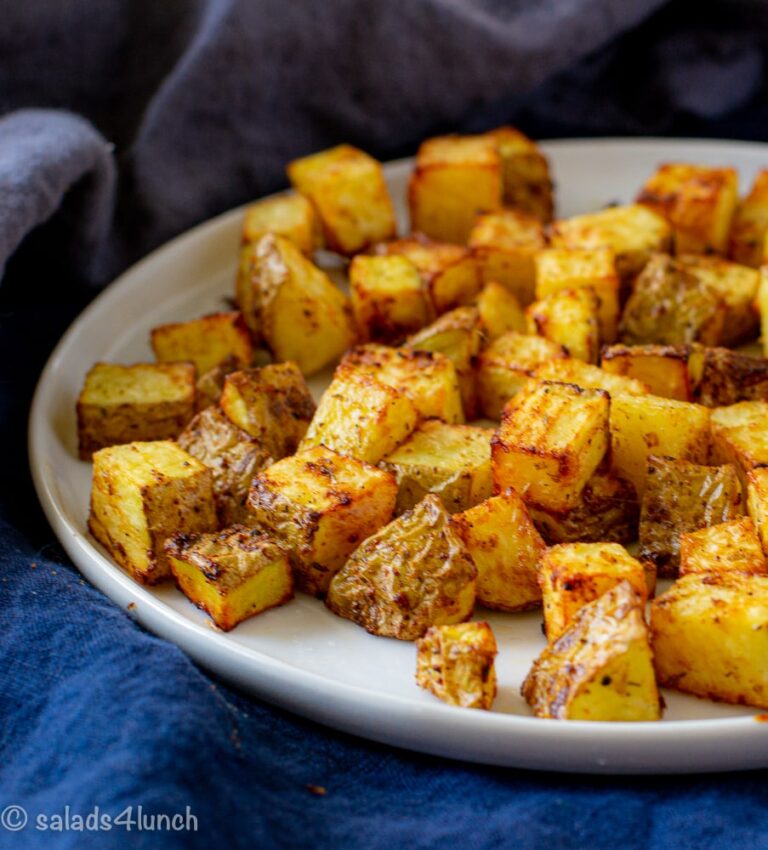 Side view of a white plate of delicious home fries on a blue napkin.