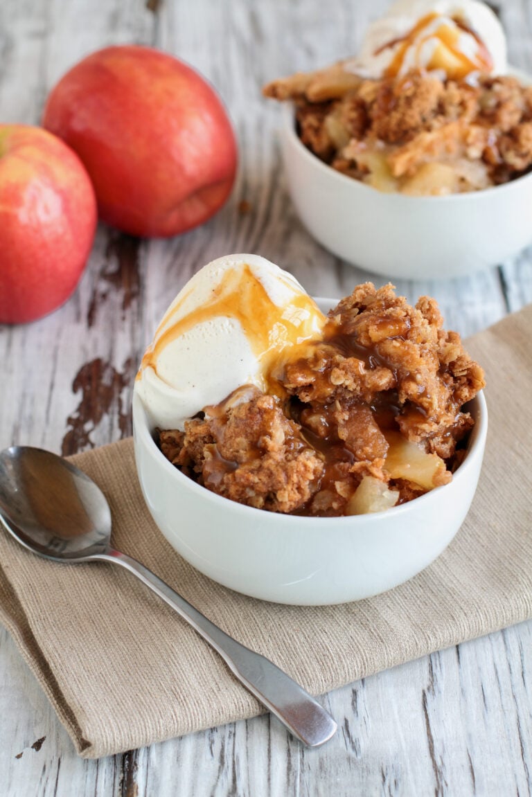 Fresh hot homemade apple crisp or crumble with crunchy streusel topping topped with vanilla bean ice cream and Caramel Sauce. Selective focus with blurred background.
