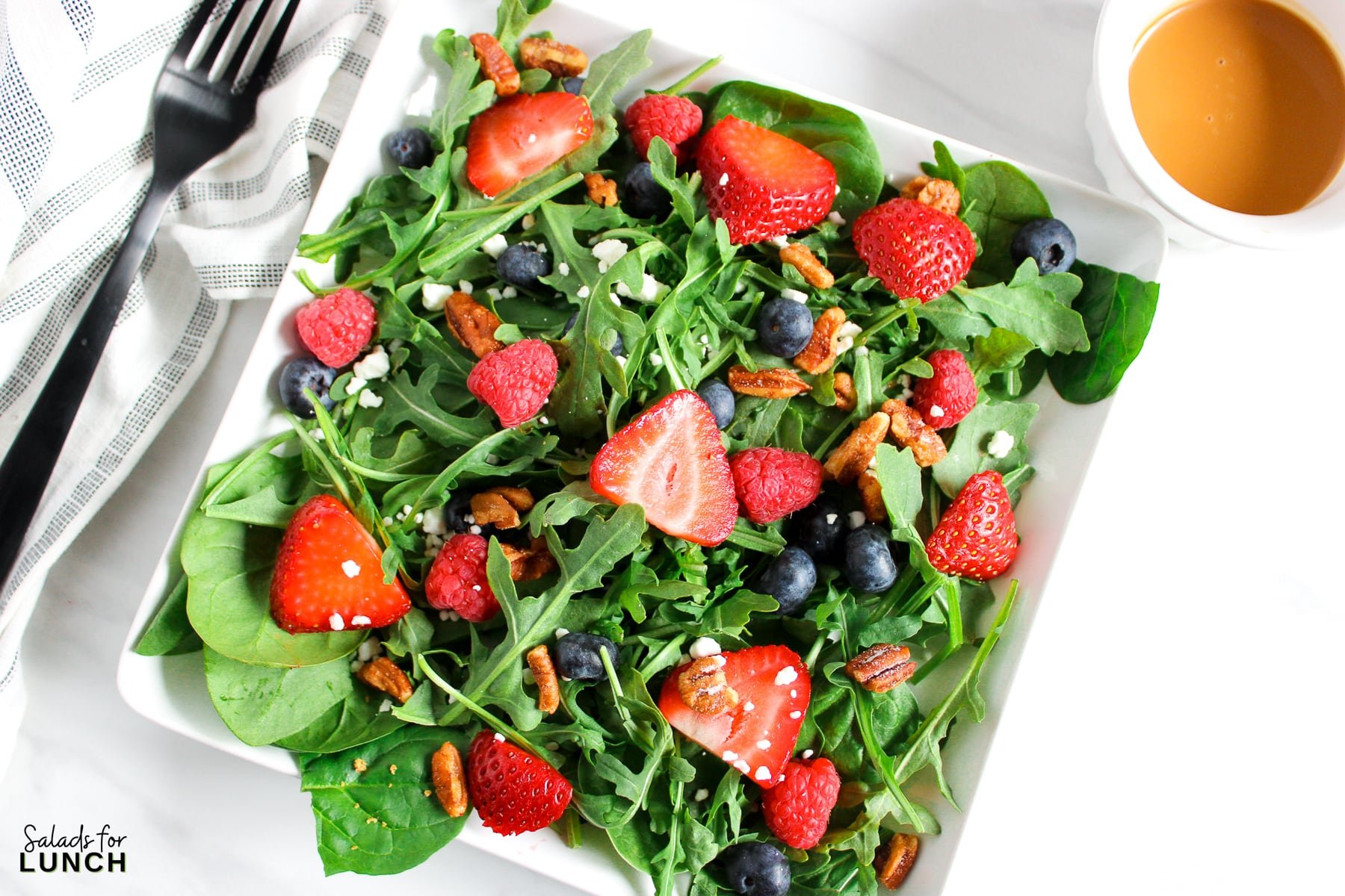 A salad with arugula,berries and honey roasted pecans topped with a creamy balsamic vinaigrette on a plate.