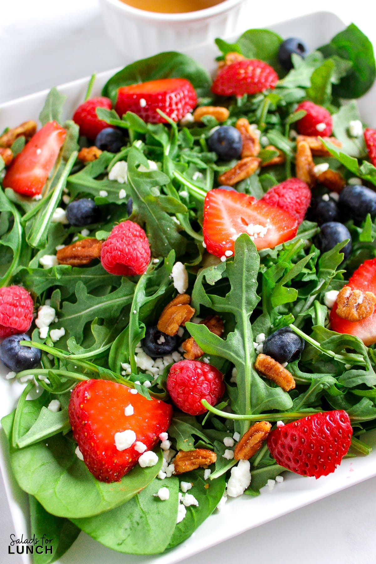 A salad with arugula,berries and honey roasted pecans topped with a creamy balsamic vinaigrette on a plate.