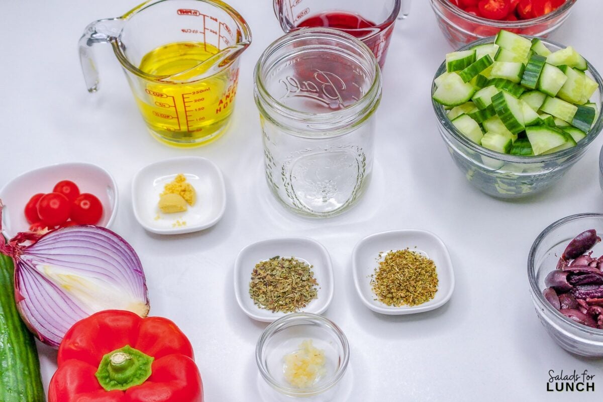 Ingredients for greek salad dressing: olive oil, red wine vinegar, salt, pepper, dried basil, dried oregano, dry mustard and minced garlic in small bowls.