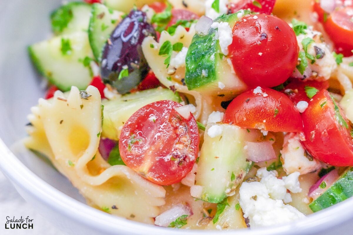 Close up of bow tie pasta with cucumbers, tomato, olives, feta cheese and greek salad dressing.