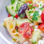Close up of bow tie pasta with cucumbers, tomato, olives, feta cheese and greek salad dressing.
