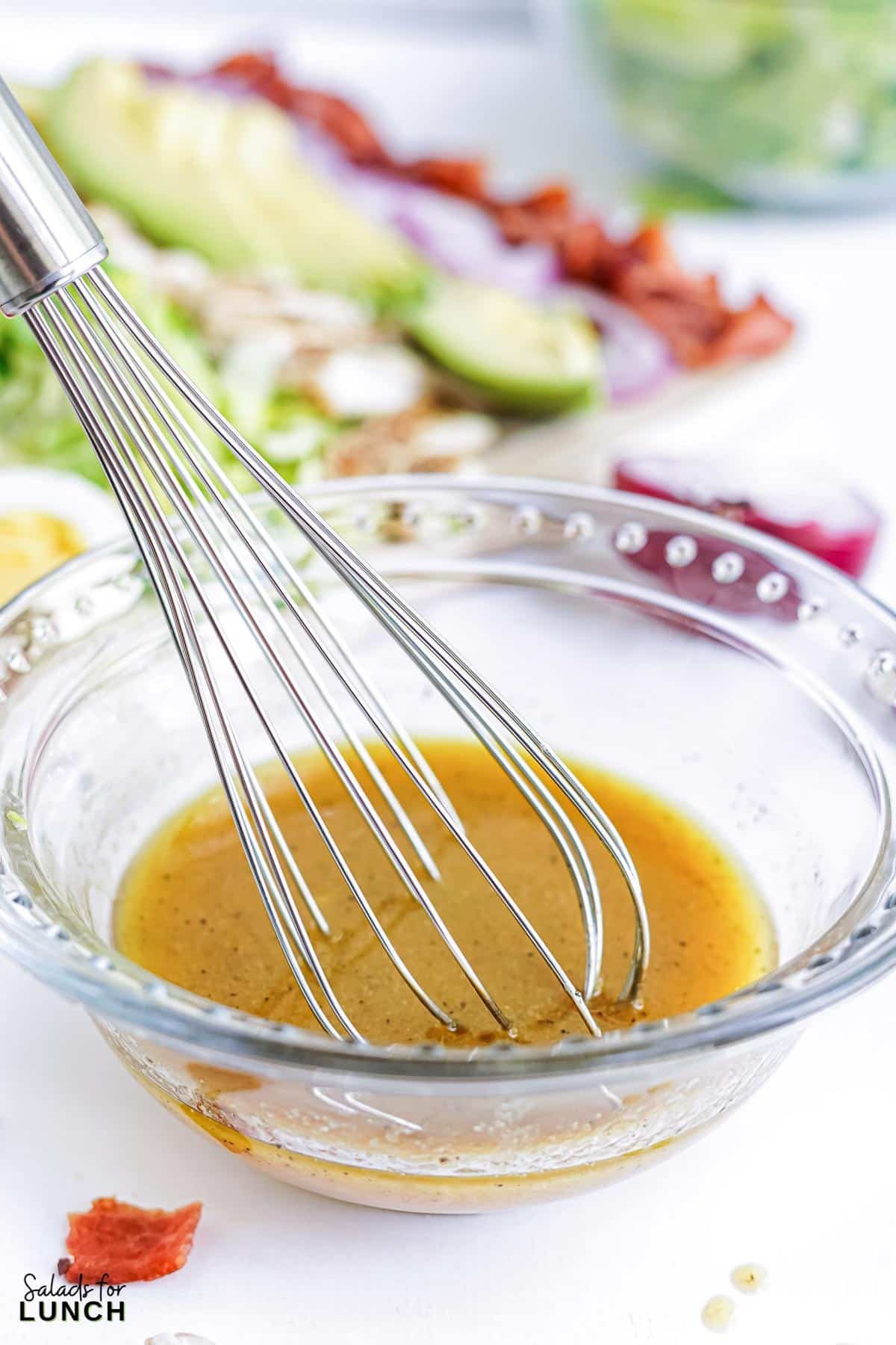 Cobb salad dressing ingredients being whisked together in a clear glass bowl.