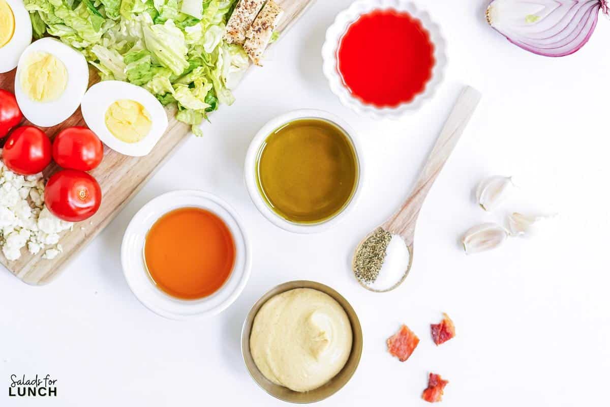 Ingredients for a classic cobb salad dressing in little bowls: Extra virgin olive oil, red wine vinegar, honey, dijon mustard, garlic, salt and pepper.