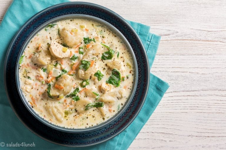 Close up of creamy gnocchi bacon soup in a blue bowl on a white table with blue napkin.
