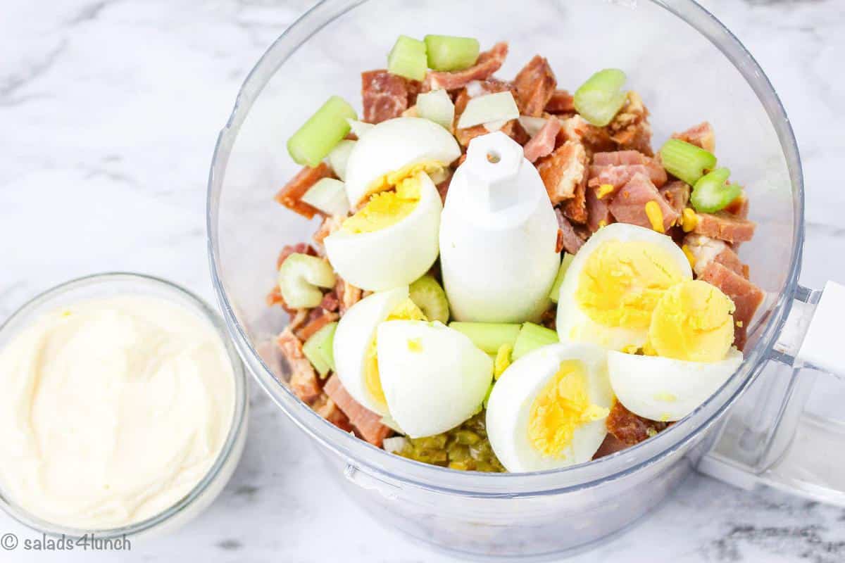 First step in deviled ham salad recipe process with ham, eggs, celery, sweet pickle relish, and onion in a food processor.