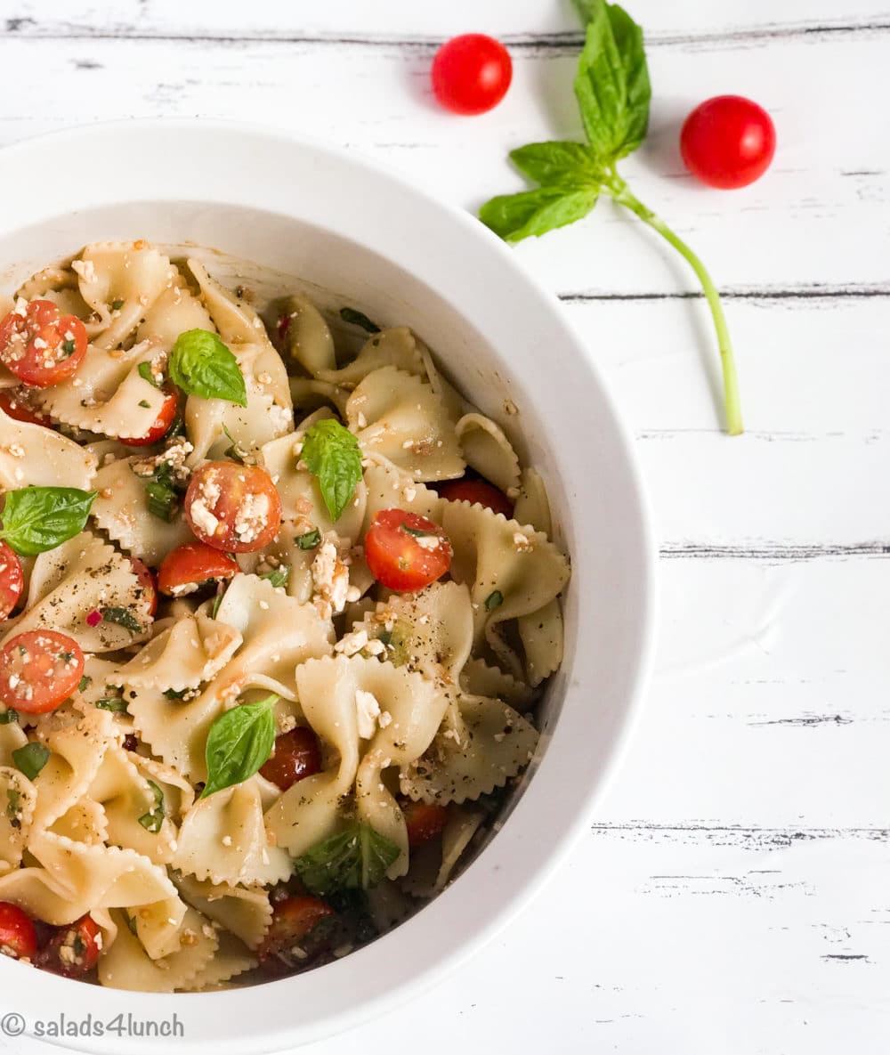 Feta Bruschetta Pasta Salad - Feta Bruschetta Pasta Salad 4 White bowl of bow tie feta bruschetta pasta salad with sprig of basil and roma tomatoes.