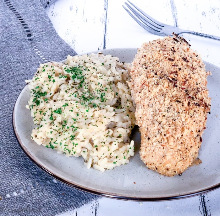 Easy Garlic Parmesan Oven Baked Chicken - Garlic Parmesan Crusted Chicken 14 Close up of garlic parmesan baked chicken breast with a side of risotto on a white plate on a grey napkin.