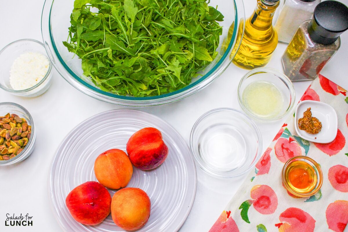 Ingredients shot of the ingredients needed to make this grilled peach salad recipe: peaches, arugula, pistachios, feta cheese, apple cider vinegar, lemon juice, olive oil, dijon mustard and honey.