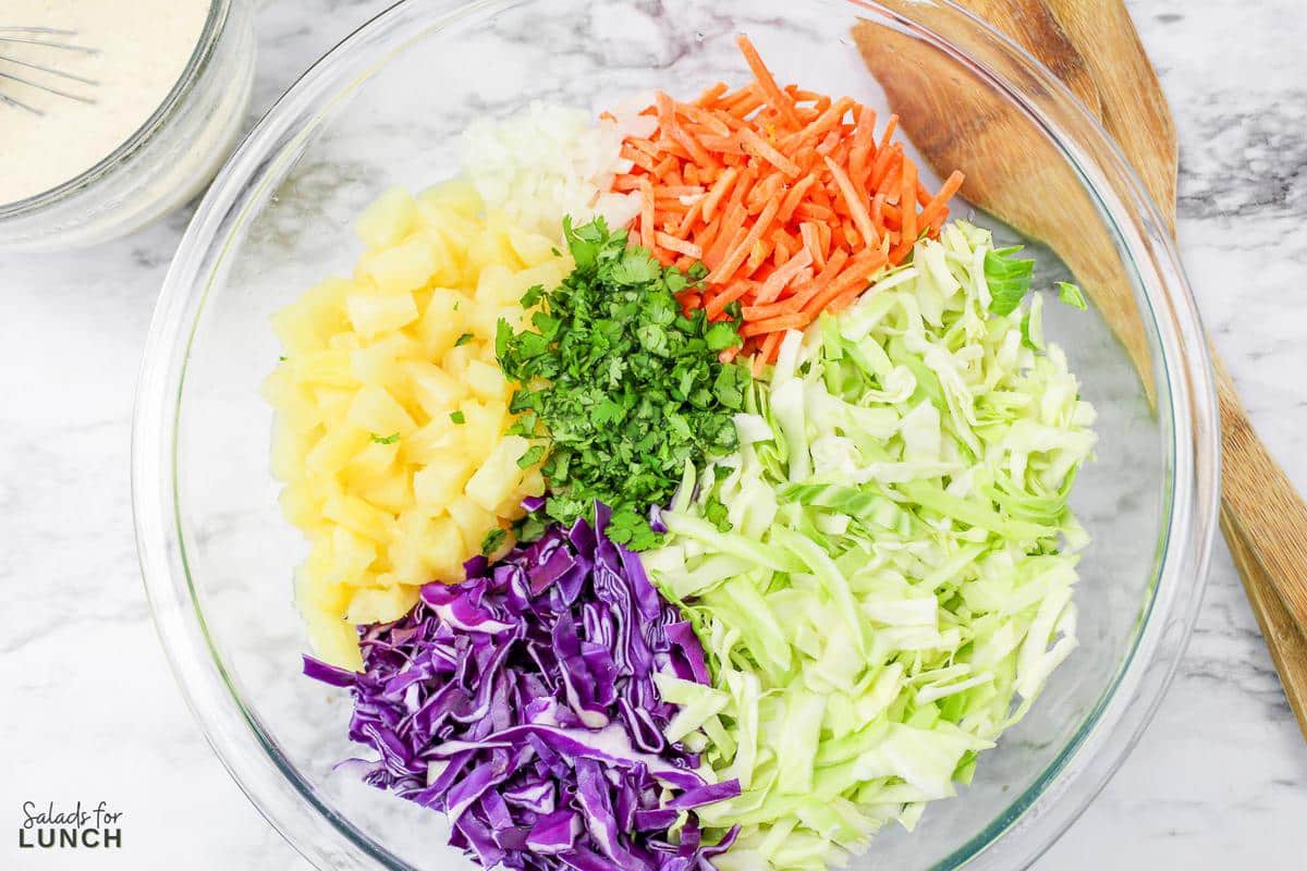 Close up of shredded cabbage, carrots, pineapple and cilantro in a bowl.