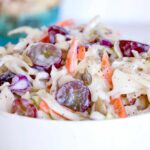 Creamy Coleslaw in a white bowl with grapes and sunflower seeds with text overlay that says: "Easy Creamy Coleslaw".