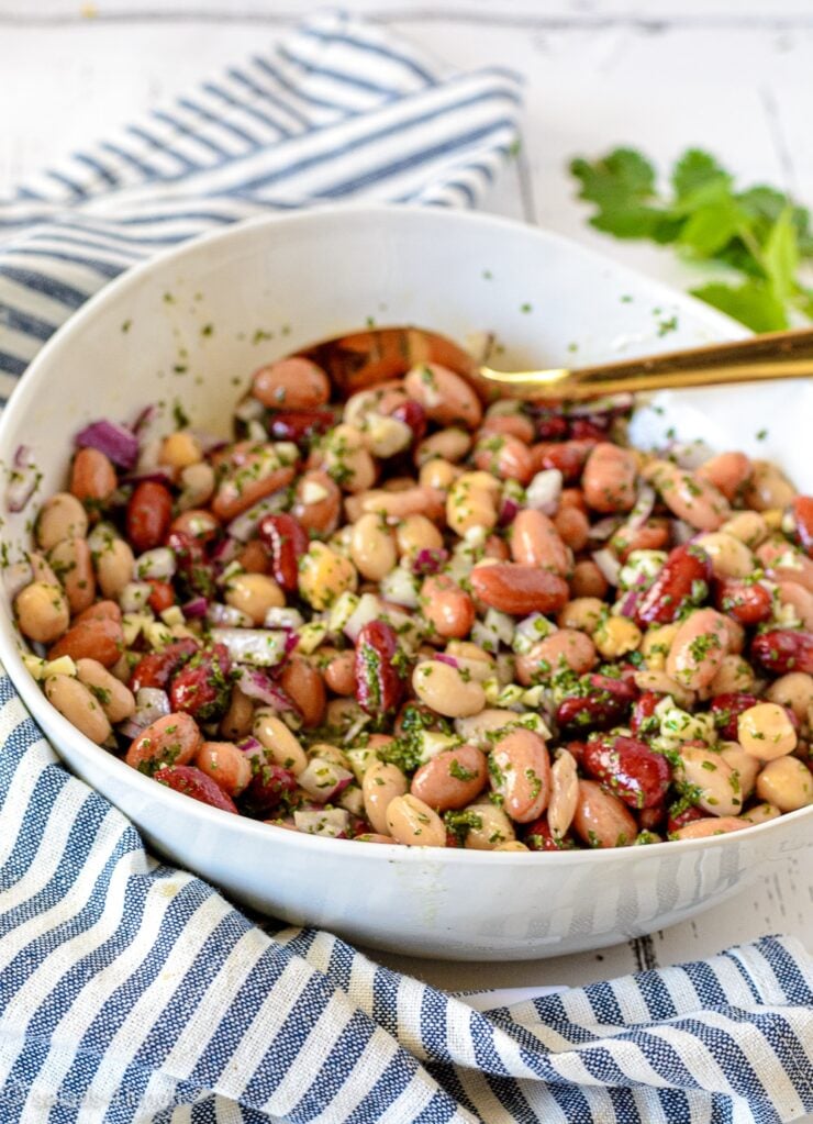 Close up of a white bowl with five bean salad in it on a blue and white striped napkin.