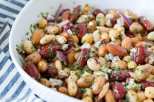 Close up of a white bowl with five bean salad in it on a blue and white striped napkin.