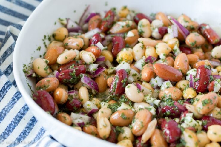 Close up of a white bowl with five bean salad in it on a blue and white striped napkin.