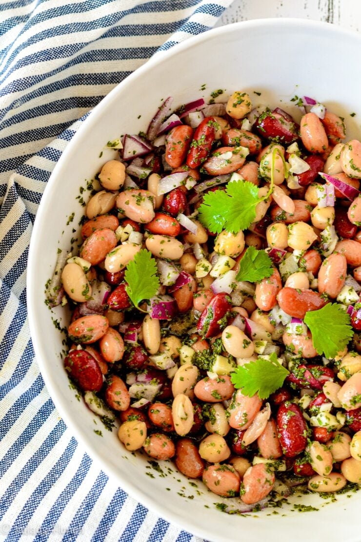 Close up of a white bowl with five bean salad in it on a blue and white striped napkin.