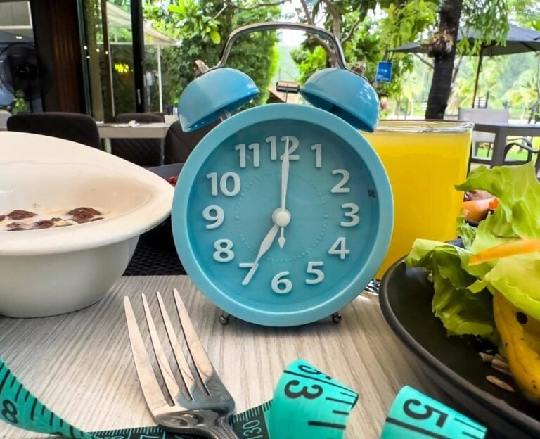 Blue clock for fasting with healthy food on a white striped table.
