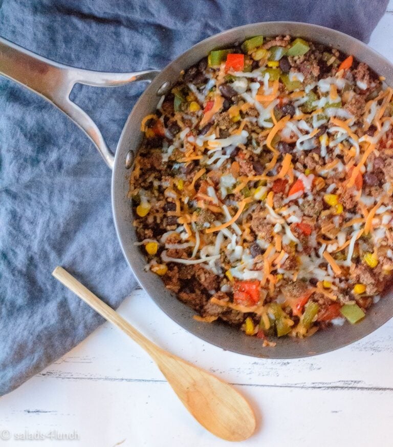 Silver skillet with Mexican Rice Casserole on a blue linen napkin with a wooden spoon to the left of the skillet,