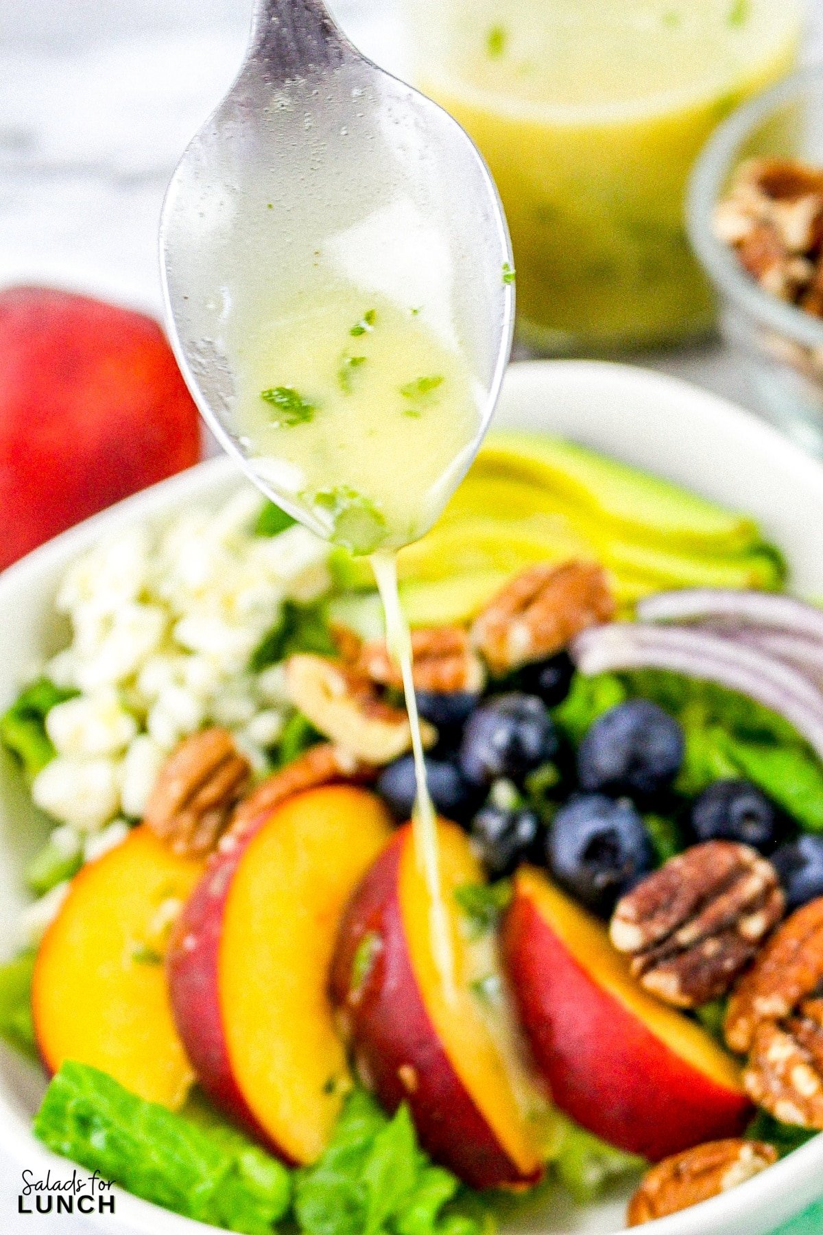 Summer Peach Salad with Fresh Mint Dressing - Peach Salad with Mint Dressing 25 Fresh mint salad dressing being drizzled from a spoon onto a summer peach salad with blueberries, avocado, onions and blue cheese.