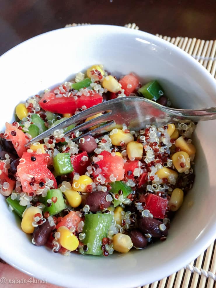 Close up of a fork in a white bowl showing quinoa salad with corn, black beans, red peppers, and green peppers.