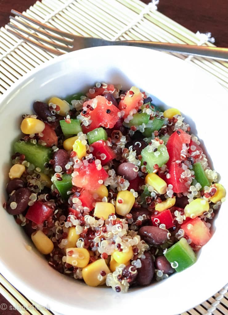 close up of white bowl showing quinoa salad with corn, black beans, red peppers, and green peppers. 