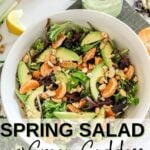 a white bowl with spring salad, mandarin oranges and cashews on a cutting board besid a mason jar with green goddess salad dressing.