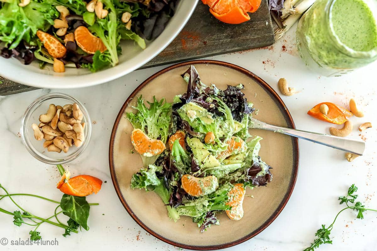 An overhead photo of a brown plate with colourful spring salad with a fork, mandarin oranges and green goddess salad dressing.