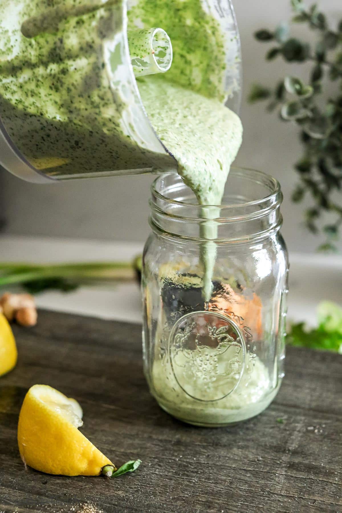 Close up of green goddess salad dressing being poured out of a food processor into a mason jar.