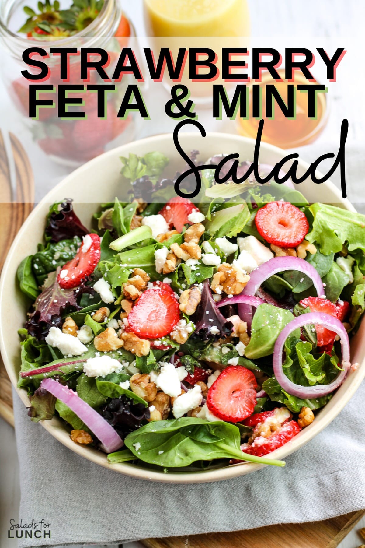 Strawberry feta and mint salad with fresh greens in a white bowl with text overlay that says "Strawberry Feta and Mint Salad".
