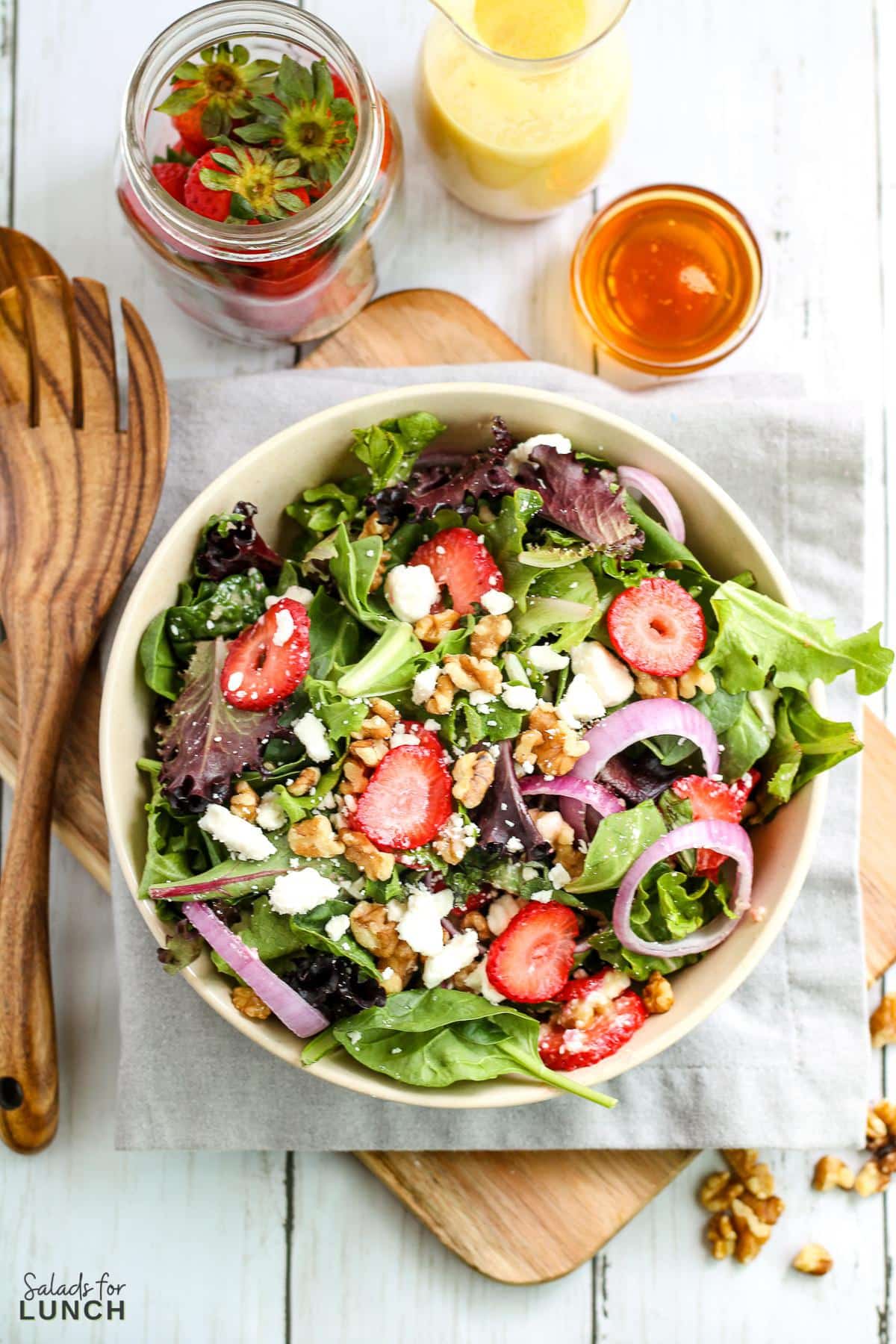 Overhead photo of a white bowl with a colourful strawberry, feta and mint salad with spring mix on a grey napkin.