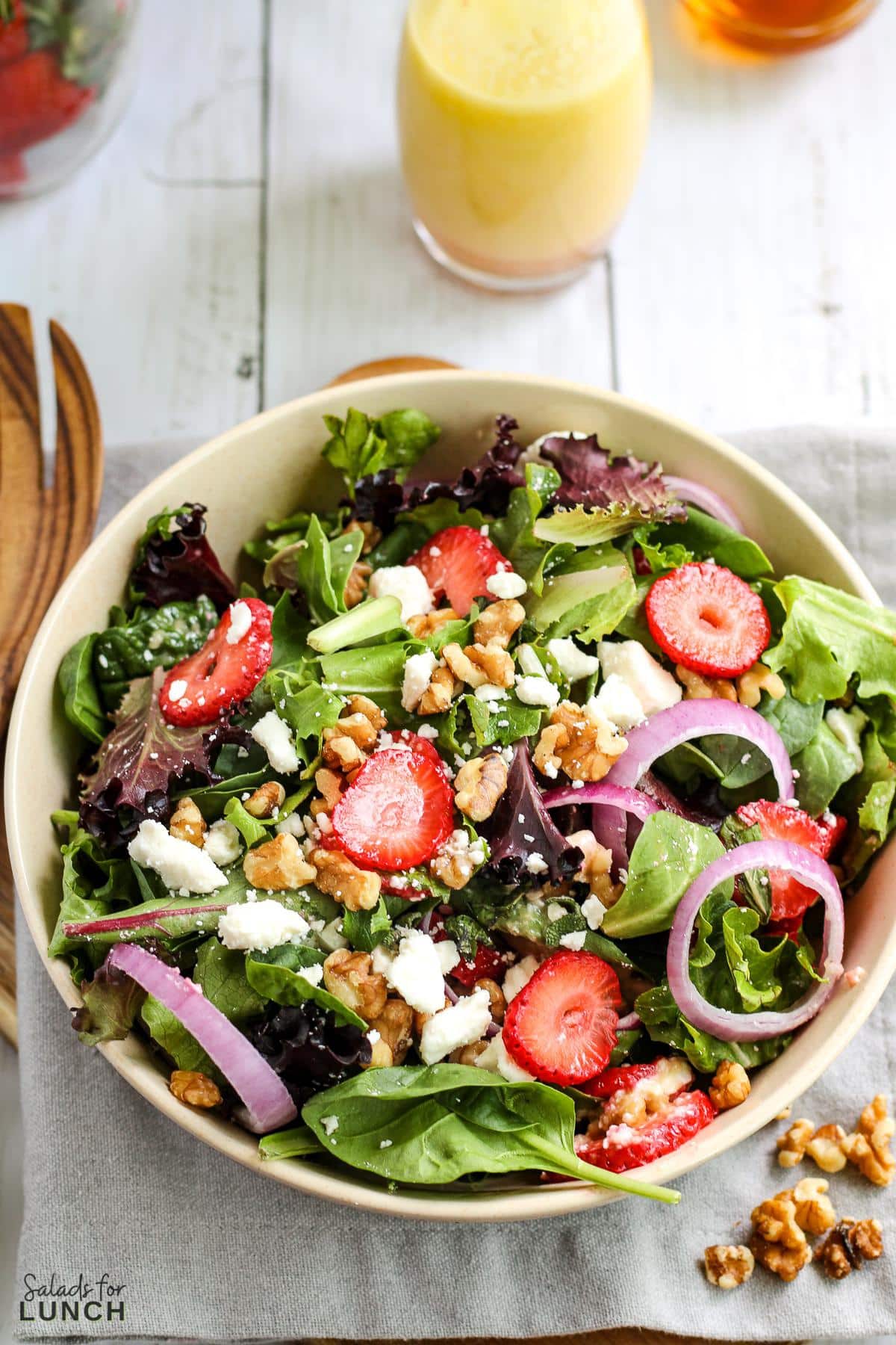 Summertime Strawberry Feta and Mint Salad - Strawberry Feta Mint Salad 13 Strawberry feta and mint salad with fresh greens in a white bowl with a wooden salad fork next to the bowl.