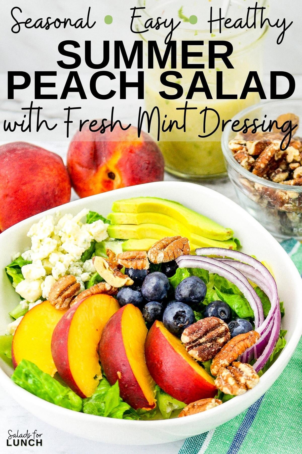 Summer peach salad with fresh peaches, blueberries, onion, romaine lettuce, pecans and blue cheese in a square white bowl with fresh mint dressing in the background on a green napkin and a white marble surface