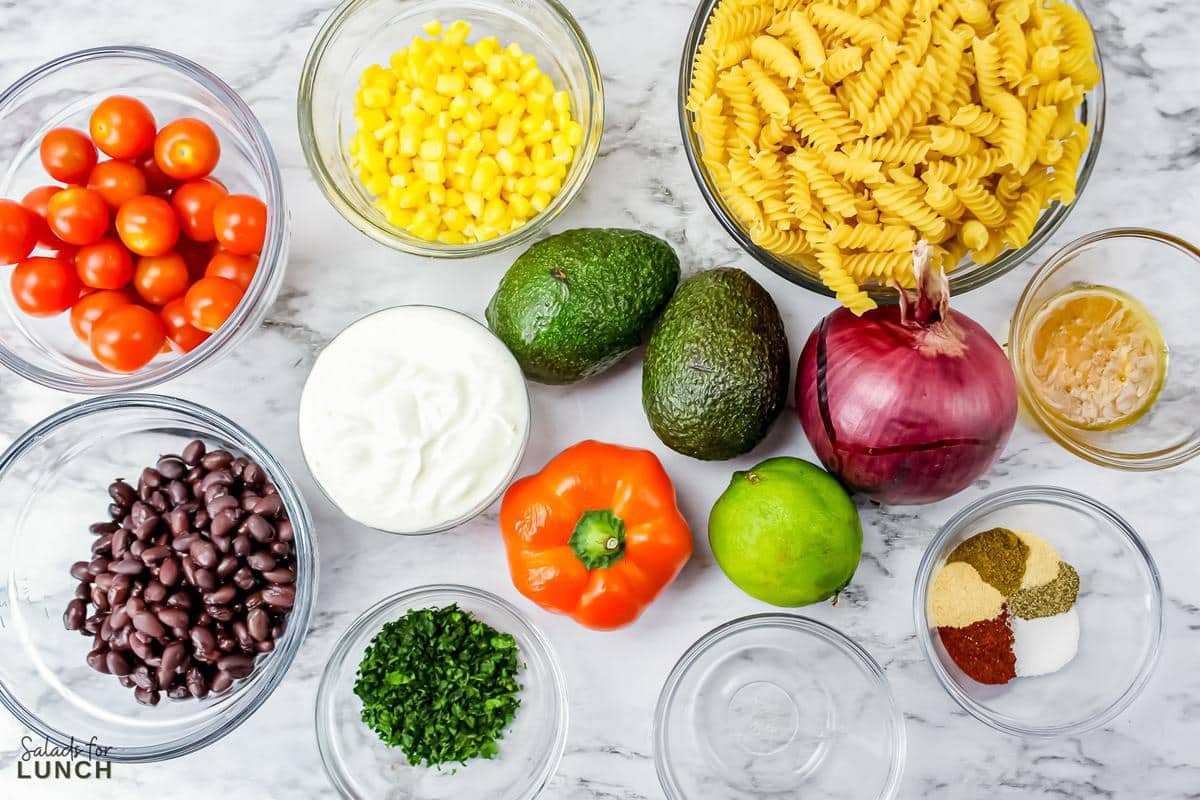 Overhead photo of taco pasta salad ingredients: pasta, corn, tomatoes, cilantro, black beans, red onion, orange pepper, and jalapenos.