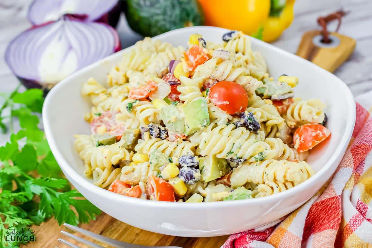 White bowl with Mexican Pasta Salad in iton a wood cutting board with colourful orange and yellow napkin beside it.