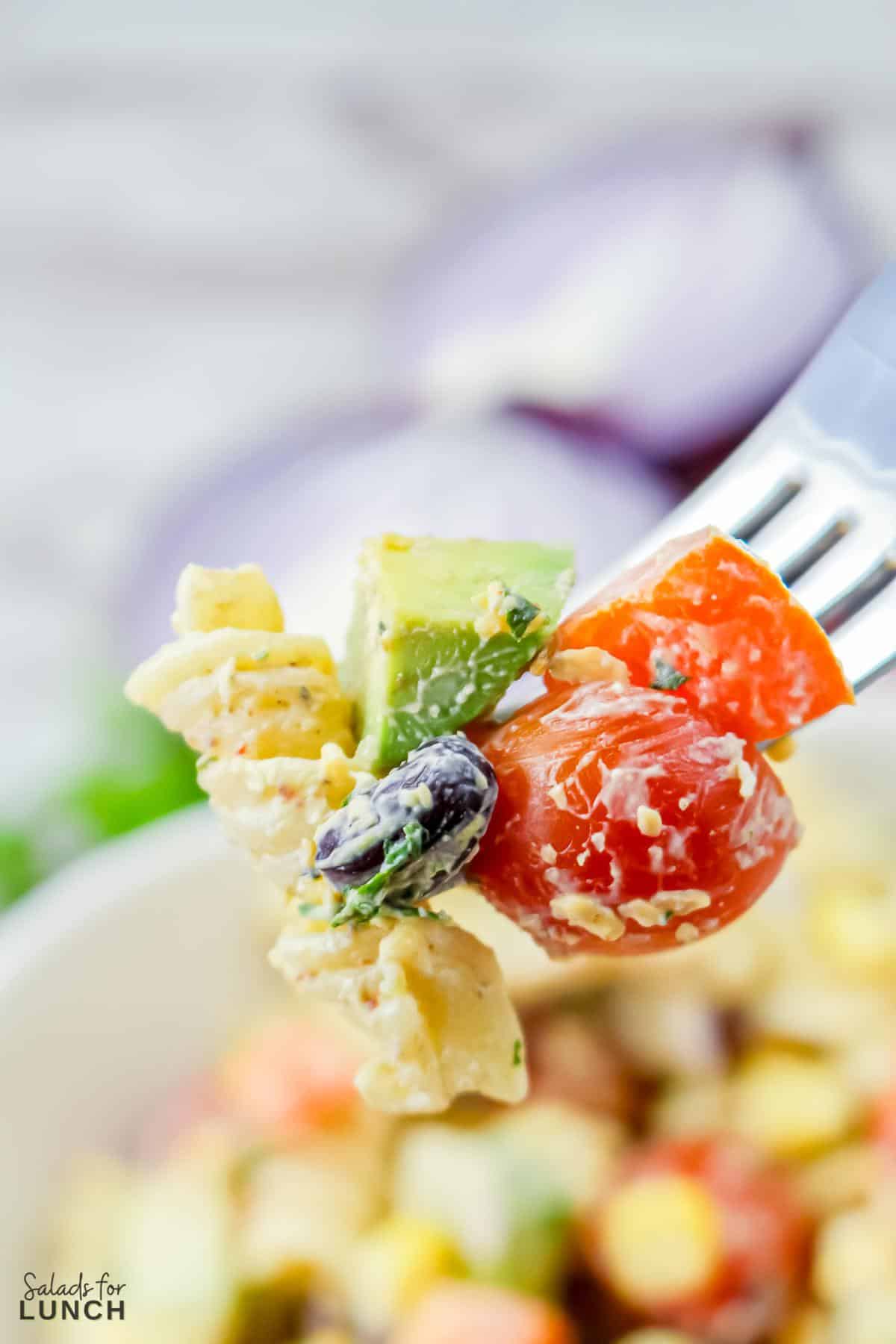 Fork with a big bite of delicious mexican pasta salad onit and a blurry bowl of pasta salad in the background.