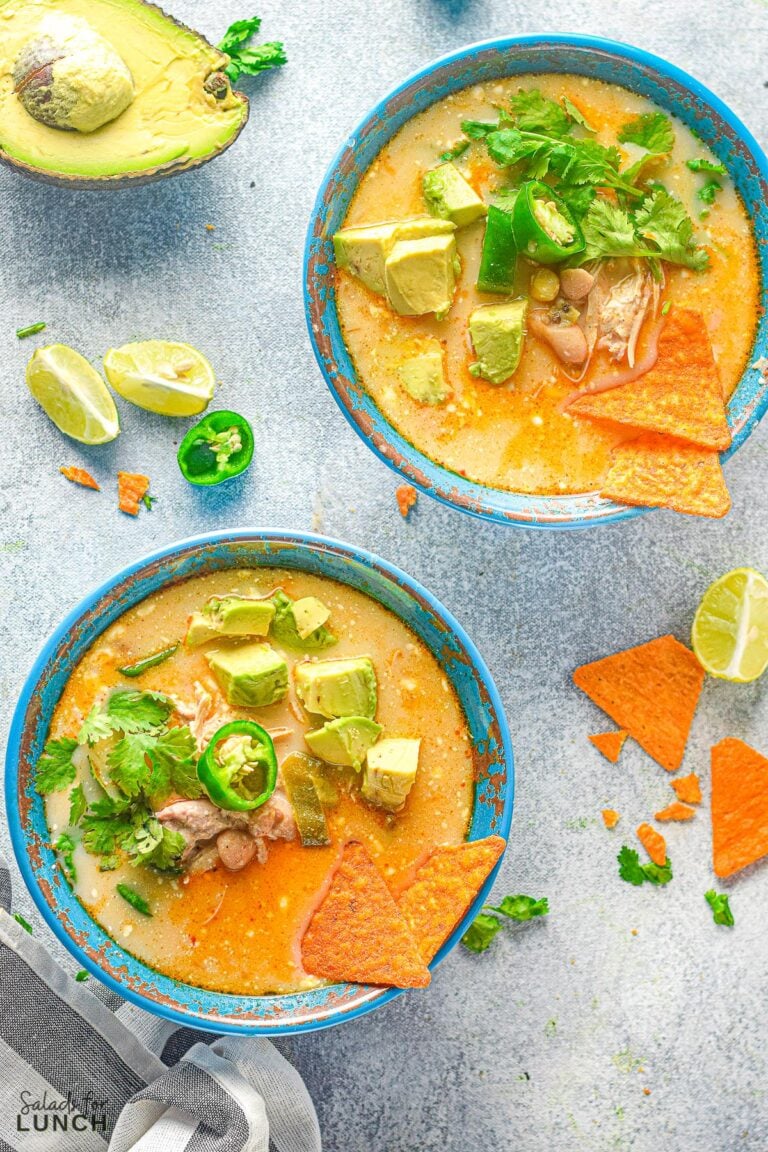 Overhead angle of two teal coloured bowls with white chicken chili garnished with sliced avocado, cilantro, a jalapeno slice and tortilla chips.