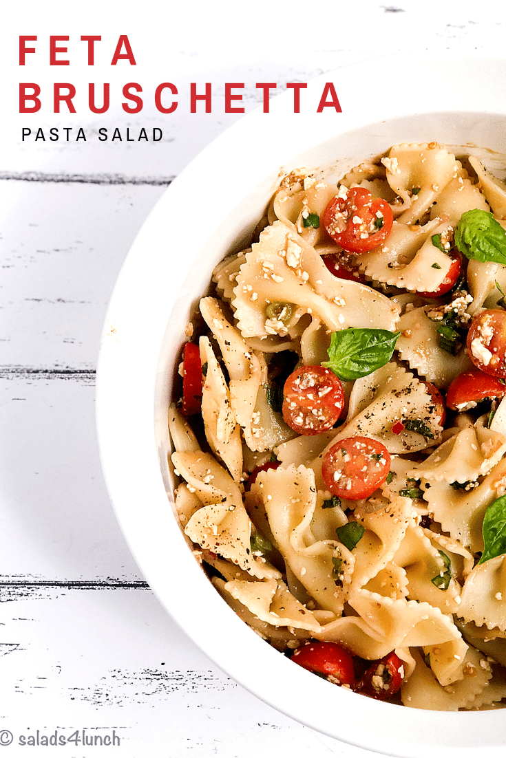 White bowl of bow tie feta bruschetta pasta salad with sprig of basil and roma tomatoes.