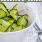 Spiralized cucumber salad with vinegar in a white bowl on a white washed wooden counter.