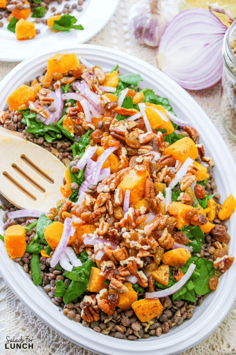 Fall salad in an oval dish with French lentils, spinach, butternut squash, toasted pecans, red onions and golden raisins layered and tossed in a delicious dressing.