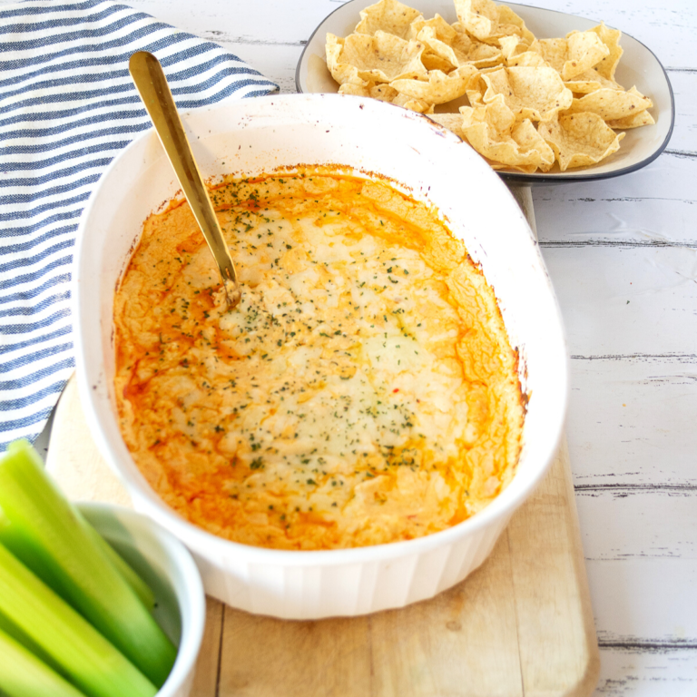 Close up of a white Corningware baking dish with buffalo chicken dip in it, sprinkled with parsley, and a bowl of tostitos and celery beside it.